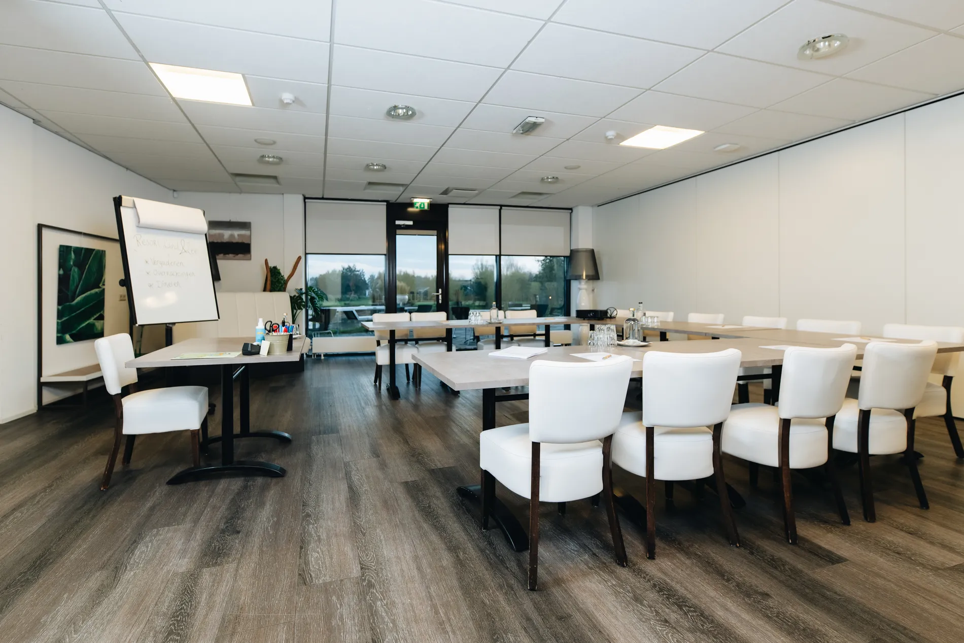 Overzicht van een professionele vergaderzaal in U-vorm opstelling met comfortabele witte stoelen en flipchart bij Resort Land & Zee.